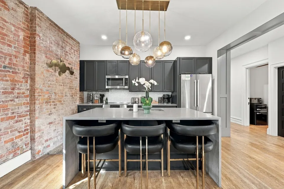 The kitchen island under globe pendants, beside the brick wall